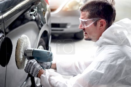 Photo for Mechanic painter man wearing protective cloth working with grinding tool for sanding of car elements. Auto mechanic painting, fixing and repairing customer car automobile at garage repair service shop - Royalty Free Image