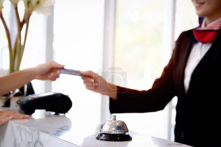 Silver bell on hotel reception service desk with blurred background of female receptionist hand reaching out for receiving credit card form customer guest at hotel, service hotel and payment concept.