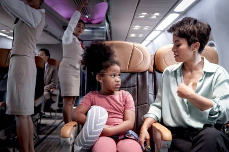 Téléchargez les photos : Cheveux bouclés fille africaine enfant passager se sentant anxieux et se soucier de voyager en avion, mère parent réconfortant fille enfant nerveux pendant assis dans un siège à l'intérieur de l'avion, transport aérien - en image libre de droit