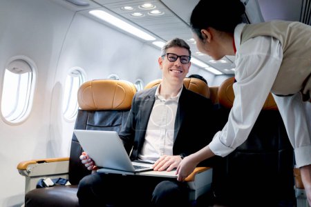 Photo for Busy businessman working on laptop computer inside airplane, air hostess warning male passenger does not use electronics device during plane takeoff and landing, traveling with airline transportation. - Royalty Free Image
