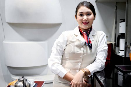 Téléchargez les photos : Portrait d'une belle hôtesse de l'air asiatique dans la cuisine de l'avion après avoir préparé de la nourriture et des boissons pour servir les passagers dans l'avion, le travail d'agent de bord, le travail de service aérien - en image libre de droit