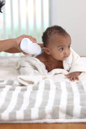 Photo for Happy African toddle baby infant covered with white towel after taking a bath in bathroom, father hand holding dusting powder bottle, dad apply talcum powder on body of little cute kid daughter child. - Royalty Free Image