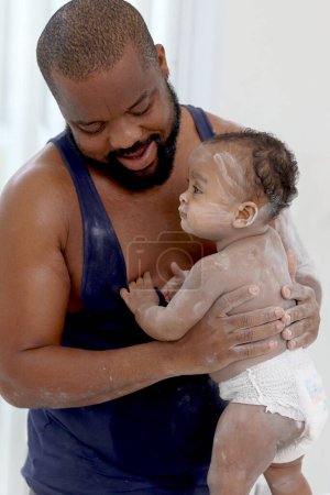 Photo for Happy African family, Father holding cute toddle baby infant kid after taking a bath and apply talcum powder on body ready in bathroom. Dad looks after little cute daughter child in family. - Royalty Free Image