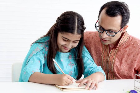 Photo for Cute Indian school student girl in India traditional dress doing homework with her father. Dad teaching daughter kid at home, parent become teacher tutor involvement in childhood education in family. - Royalty Free Image