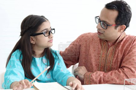 Photo for Cute Indian school student girl in India traditional dress doing homework with her father. Dad teaching daughter kid at home, parent become teacher tutor involvement in childhood education in family. - Royalty Free Image