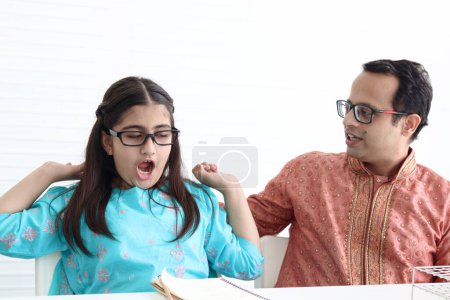 Photo for Indian school student girl in India traditional dress yawning during doing homework with father. Dad teach sleepy daughter kid, parent become teacher tutor involvement in childhood education in family - Royalty Free Image