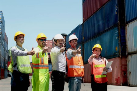 Group of worker team with helmet and safety vest stand in line and give thumbs up at logistic shipping container yard. Woman and men workmate engineers working together at workplace.