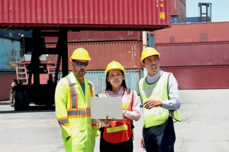 Asiatische Arbeiterinnen mit Helm und Sicherheitsweste diskutieren per Laptop mit Kollegen auf der Logistik-Containerwerft über Ergebnisse. Frauen und Männer arbeiten im Ingenieurteam zusammen.