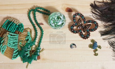 Foto de Plumas de pavo real con perlas verdes y broche de mariposa verde y cobre en la mesa de madera - Imagen libre de derechos