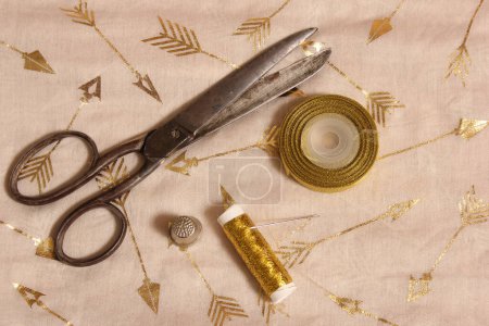 Spule aus Goldfaden und Schere mit Fingerhut auf metallischem Chiffongewebe