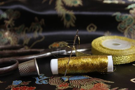 Téléchargez les photos : Bobine de fil d'or avec dé à coudre sur tissu de soie asiatique noir - en image libre de droit