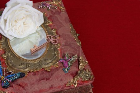 Antikes Märchenbuch mit Juwelen und weißer Rose auf rotem Samt