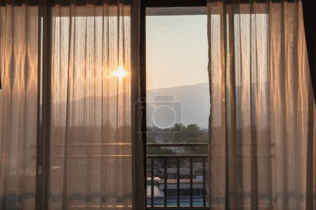 Photo for Views from inside the rooms through the curtains that cover the window panes outward offer views of the mountains and the rising sun in the summer after a restful night. - Royalty Free Image