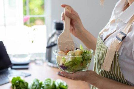 Photo for Young woman is making salad from vegetables she has prepared on table in her home kitchen to get salad that is clean and safe because ingredients are carefully selected. healthy food preparation ideas - Royalty Free Image
