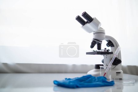 Foto de Guantes médicos y microscopio se colocan sobre la mesa en el laboratorio para preparar virólogos que quieren utilizar el laboratorio para examinar las muestras de virus que recibieron de la epidemia. Equipos médicos para su uso en el laboratorio - Imagen libre de derechos
