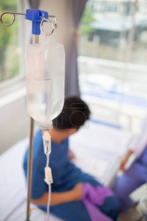 An iron stand to hang saline bottle high to deliver saline via catheter to an intravenous patient lying on patient bed. Medical concept in which doctor gives saline solution to patient through vein