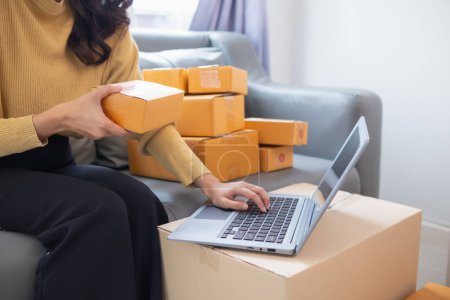 businesswoman decides invest in small SME business at home by using laptop and smartphone do online marketing and sell things online through an application before packing products according to orders.