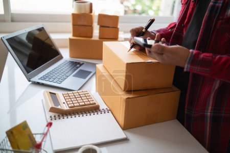 businessman decides invest in small SME business at home by using laptop and smartphone do online marketing and sell things online through an application before packing products according to orders.
