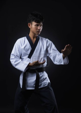 Male black belt taekwondo instructor in white uniorm teaches standing poses on black background