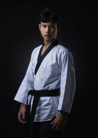 Taekwondo-Instruktor mit schwarzem Gürtel in weißer Uniform posiert und schaut geradeaus auf schwarzem Hintergrund