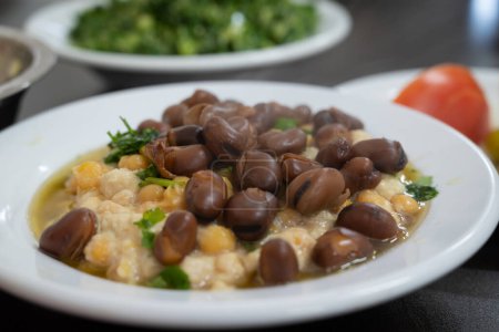 Photo for Hummus, a traditional Middle eastern Arabic style mashed chickpeas dish, with baked beans of Vicia Faba, served in a white bowl with olive oil - Royalty Free Image
