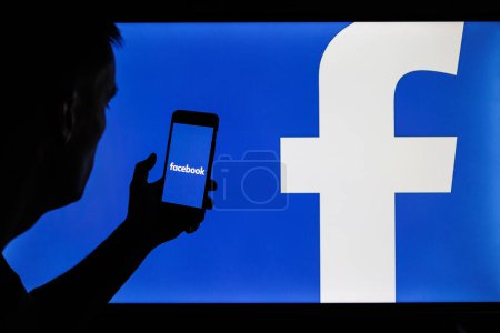 Photo for Vilnius, Lithuania - 2022 February 6: Facebook and Meta company logo on smartphone and PC screens. Man silhouette holding facebook app in hand - Royalty Free Image