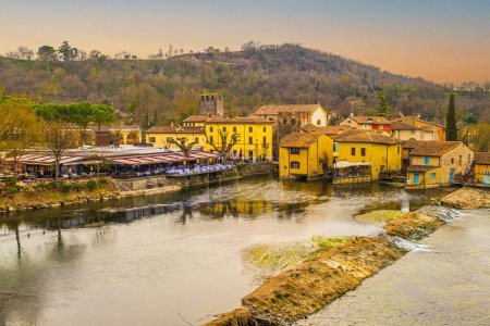 Téléchargez les photos : Valeggio, Italie - 03-02-2022 : Vue en angle élevé de Borghetto sul Mincio avec les bâtiments réfléchissant sur l'eau au coucher du soleil - en image libre de droit