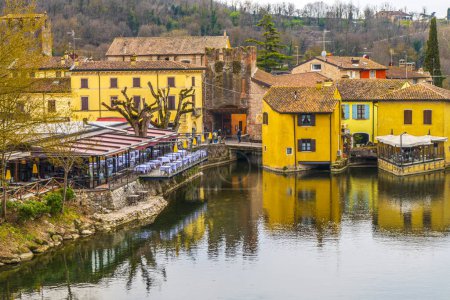 Téléchargez les photos : Valeggio, Italie - 03-02-2022 : Vue en angle élevé de borghetto sul Mincio avec les bâtiments réfléchissant sur l'eau - en image libre de droit