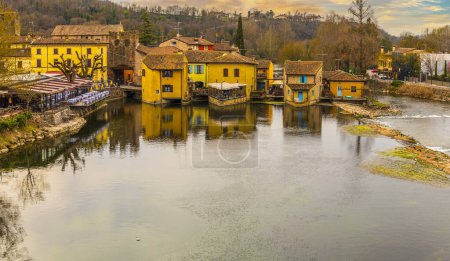 Téléchargez les photos : Valeggio, Italie - 03-02-2022 : Vue en angle élevé de Valeggio sul Mincio avec les bâtiments réfléchissant sur l'eau au coucher du soleil - en image libre de droit
