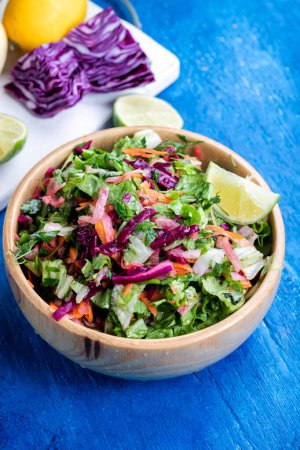 Photo for Fresh vegetable salad with purple cabbage, white cabbage, lettuce, and carrot, in a wooden bowl on a blue wooden background. - Royalty Free Image