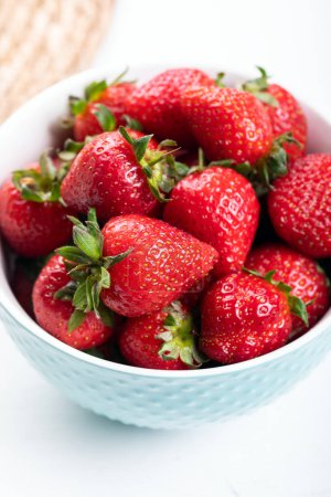 Photo for Fresh strawberries in a blue ceramic bowl, on a white table. - Royalty Free Image