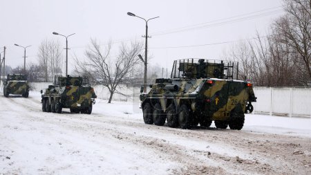 Foto de Kharkiv, Ucrania - 31 de enero de 2022: Varios transportes blindados de personal conducen a lo largo de una carretera cubierta de nieve a lo largo de un muro de hormigón. El ejército ucraniano está preparando una contraofensiva. Guerra ruso-ucraniana - Imagen libre de derechos