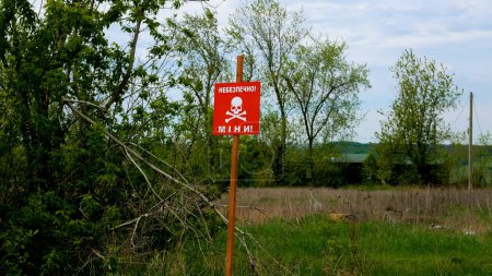 Ein rotes Schild mit der Aufschrift Danger, Minen warnt auf dem Feld in der Nähe der Straße in den nicht besetzten Gebieten vor Gefahren. Russisch-ukrainischer Krieg 2022-2023