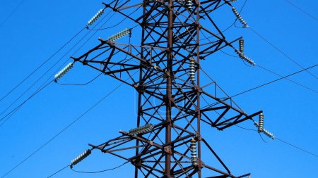 A large metal pole of a high-voltage power line against a blue sky. Production and transportation of electricity. Electricity tariffs