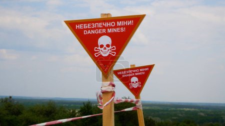 Photo for Signs with the warning inscription Danger, mines and fencing tapes in front of the settlement. Mined areas in Ukrainian villages. Russian-Ukrainian War 2022-2023. The concept of humanitarian demining - Royalty Free Image