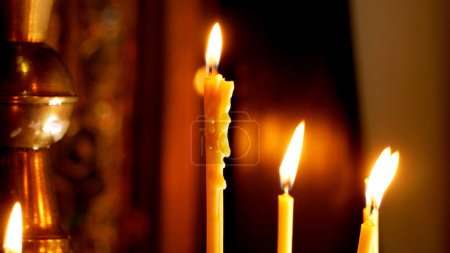 Foto de Una mano de mujer pone una vela encendida cerca de una cruz ortodoxa en una iglesia. Oración, adoración en la iglesia - Imagen libre de derechos