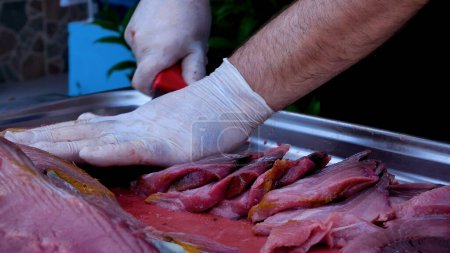 Téléchargez les photos : Les mains d'un chef ganté coupent un gros morceau de viande de poisson. Griller de la viande. De la nourriture. Pique-nique en plein air - en image libre de droit