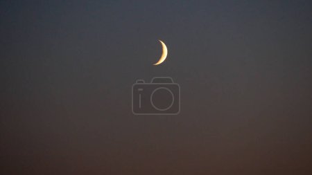 Foto de Una luna joven en un cielo oscuro. La primera aparición de la Luna en el cielo después de la Luna Nueva en forma de una media luna estrecha. - Imagen libre de derechos