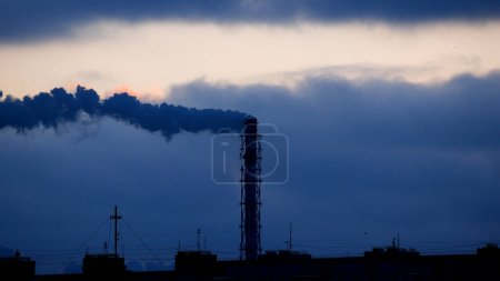 Photo for Thick smoke bills from a tall chimney against a dark sky. Industrial landscape. Operation of the thermal power plant. Heat production at a thermal power plant. - Royalty Free Image