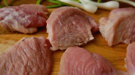 Chunks of raw pork meat on a wooden kitchen board. In the background are green onion feathers. Cooking meat dishes.