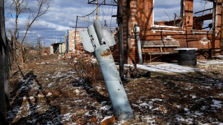 Im Hof eines zerstörten Hauses in einem ukrainischen Dorf ragt ein Projektil einer Mehrfachabschussrakete aus dem Boden. Folgen des Beschusses einer