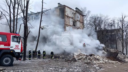 Foto de Kharkiv, Ucrania - 23 de enero de 2024: Los rescatistas están en una montaña de escombros cerca de la entrada colapsada de un edificio residencial de varios pisos en una ciudad ucraniana. Consecuencias de un ataque con misiles - Imagen libre de derechos