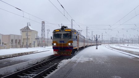 Foto de Lviv, Ucrania - 04 de enero de 2024: Un tren de pasajeros llega a la plataforma de la estación de tren. Hay nieve en la plataforma. Viajar en tren en invierno. - Imagen libre de derechos
