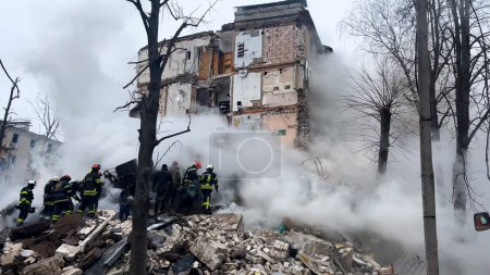 Foto de Kharkiv, Ucrania - 23 de enero de 2024: Fuego, mucho humo cerca de la entrada de un edificio residencial que se derrumbó después de un ataque con misiles. Una operación de rescate está en marcha, los rescatistas están buscando - Imagen libre de derechos