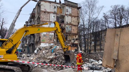 Foto de Kharkiv, Ucrania - 23 de enero de 2024: Una excavadora limpia los escombros de un edificio residencial colapsado. Las consecuencias de un ataque con misiles a un edificio residencial en una ciudad ucraniana. Ruso - Imagen libre de derechos