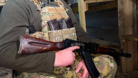 Un soldat dans un gilet pare-balles avec une mitrailleuse est assis dans un étang-réservoir. Prêt au combat avant la bataille. Le soldat est prêt à tirer. Guerre russo-ukrainienne.