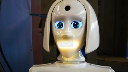 A humanoid robot made of white plastic bends over, turns its head, speaks, and flashes lights. Artificial intelligence as a human assistant. Robo-consultant.