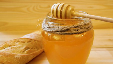A wooden spoon is dipped into a jar of liquid flowing yellow honey. Honey drips from a wooden spoon. A sweet treat.