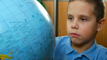 Der Junge blickt sorgfältig auf den Globus, dreht ihn, studiert Länder und Geografie. Studium der Geographie in der Schule. Ein neugieriges Kind studiert eine Weltkarte.