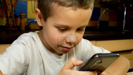 A cute boy of 7-8 years old sits with a smartphone in his hands, communicates in social networks. Child and gadgets. Distance learning. Smartphone games.